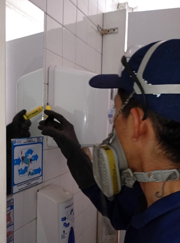 Técnico de Sergecol saneamiento ambiental realizando mantenimiento en un baño, usando guantes, mascarilla y herramientas de seguridad